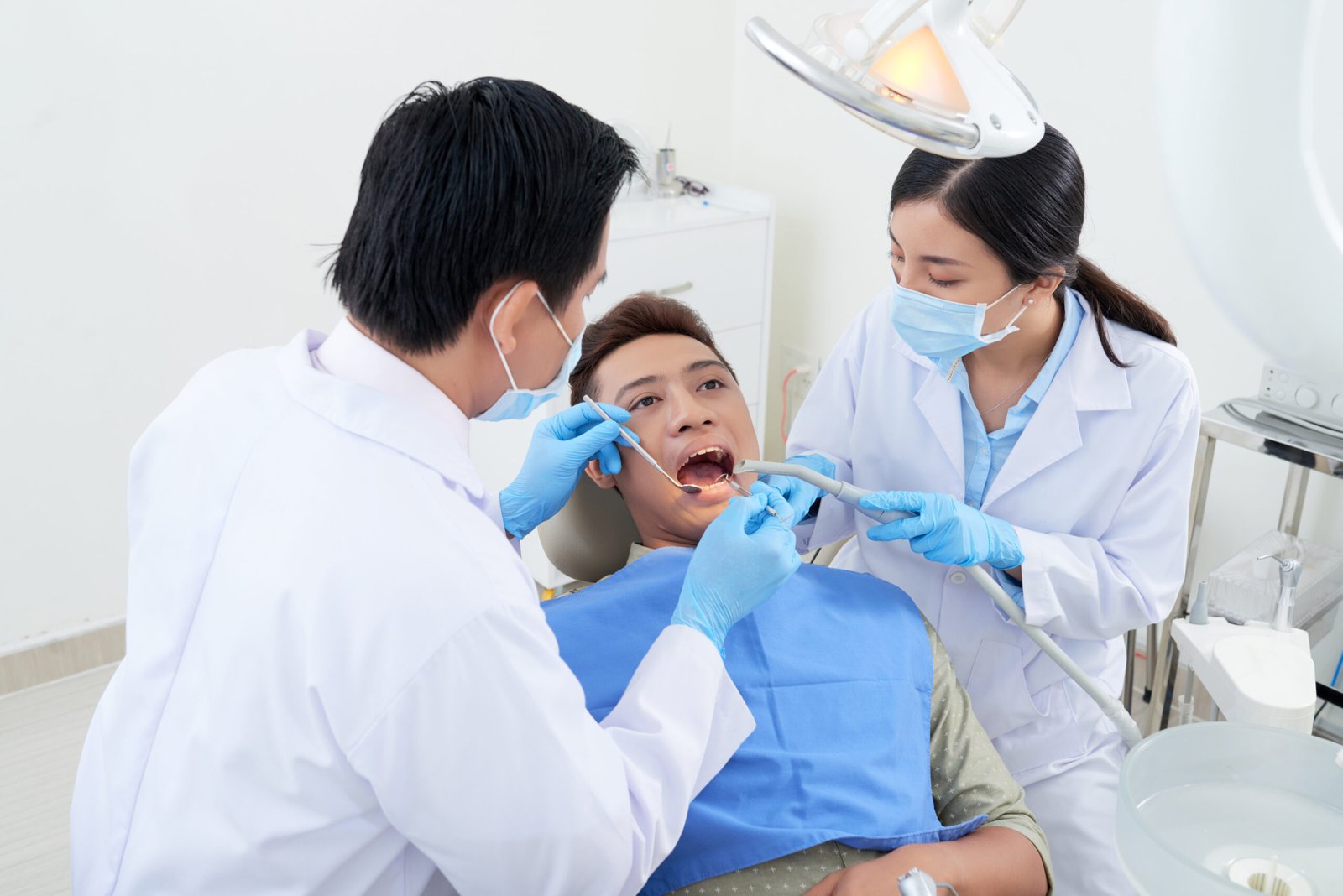 Dentist and nurse using mouth mirror, suction tube and dental explorer when examining teeth of patient